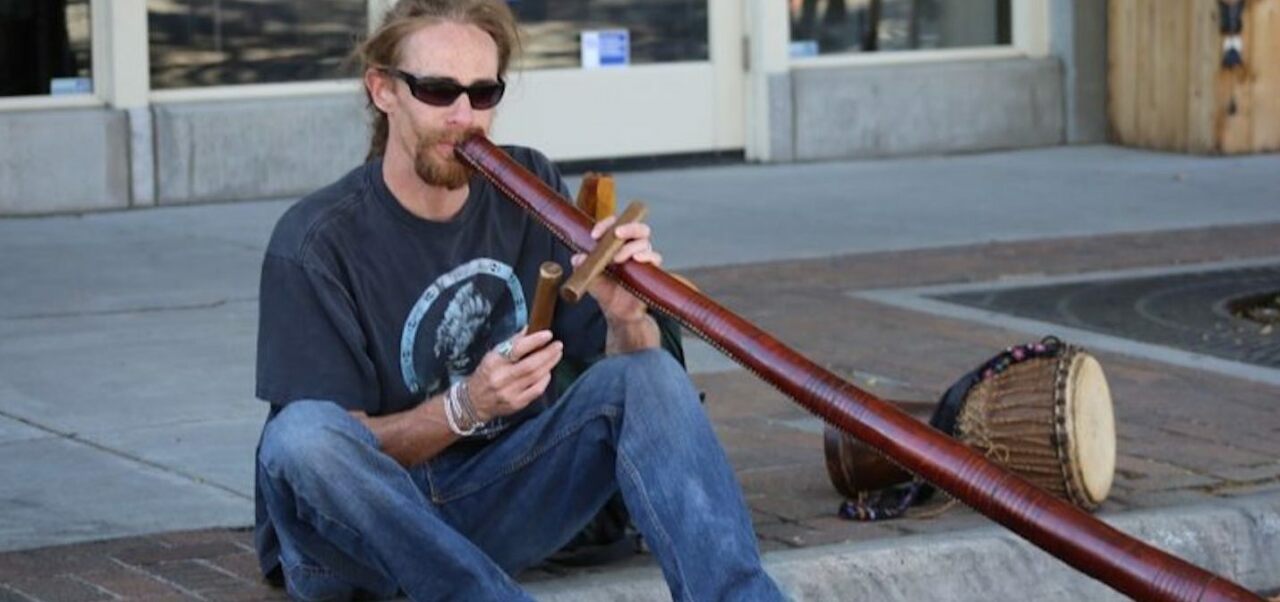 Didgeridoo spielender Mann sitzt auf dem Bürgersteig